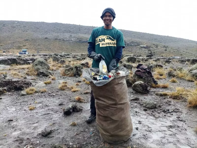 One of Team Kilimanjaro's 'Green Porters' collecting rubbish discarded by other groups on Kilimanjaro.
